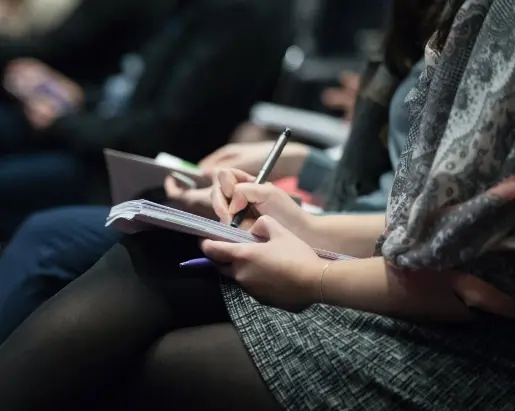 Image of a woman attending a conference or meeting, taking notes in a notepad
